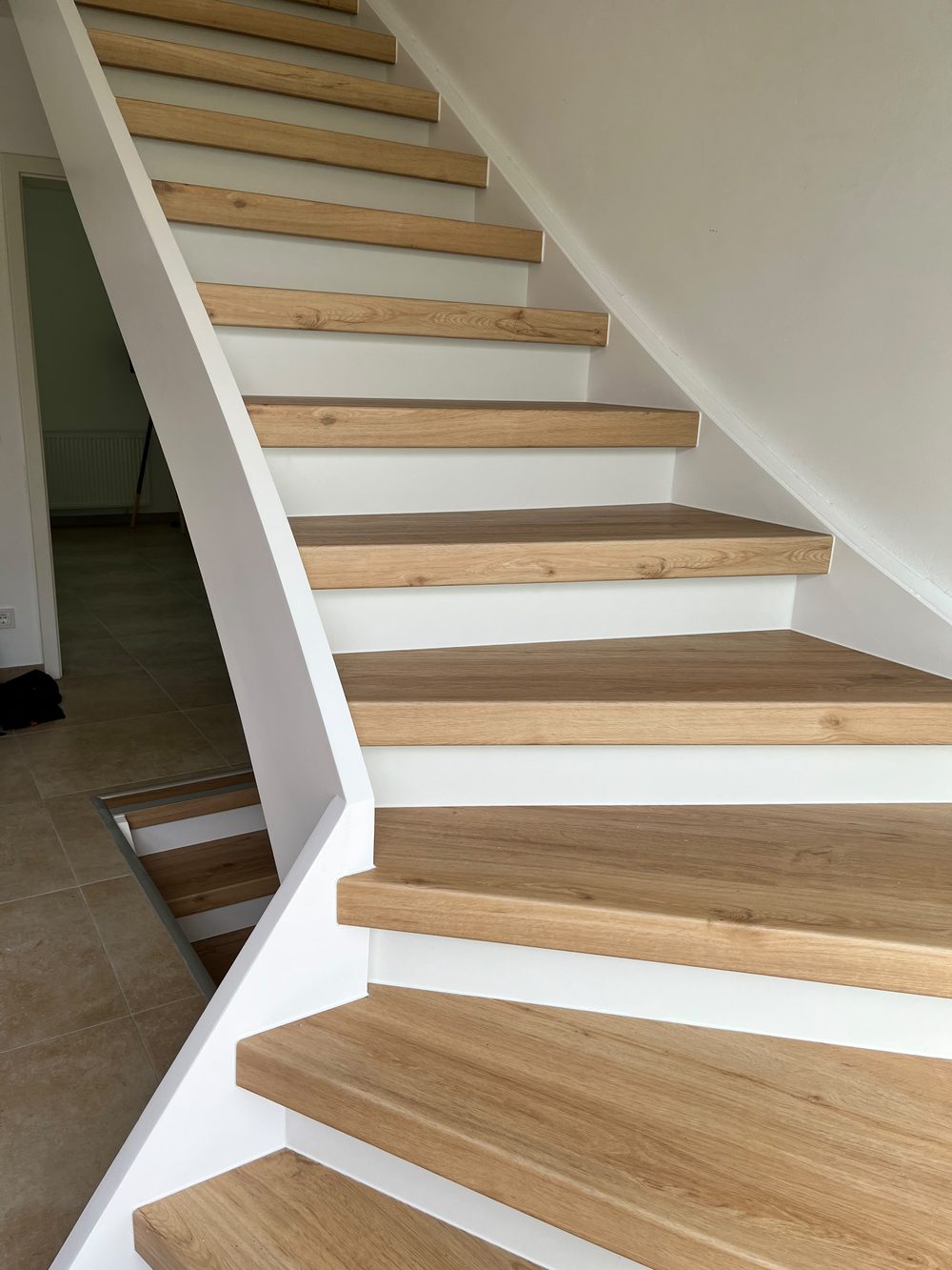 Heller Treppenaufgang mit Holzstufen und weißem Geländer
