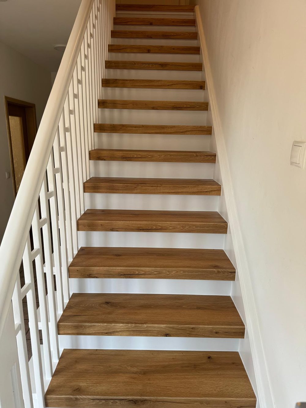Die renovierte Treppe mit hellen Holzstufen, weißen Stellstufen und weiß lackiertem Geländer