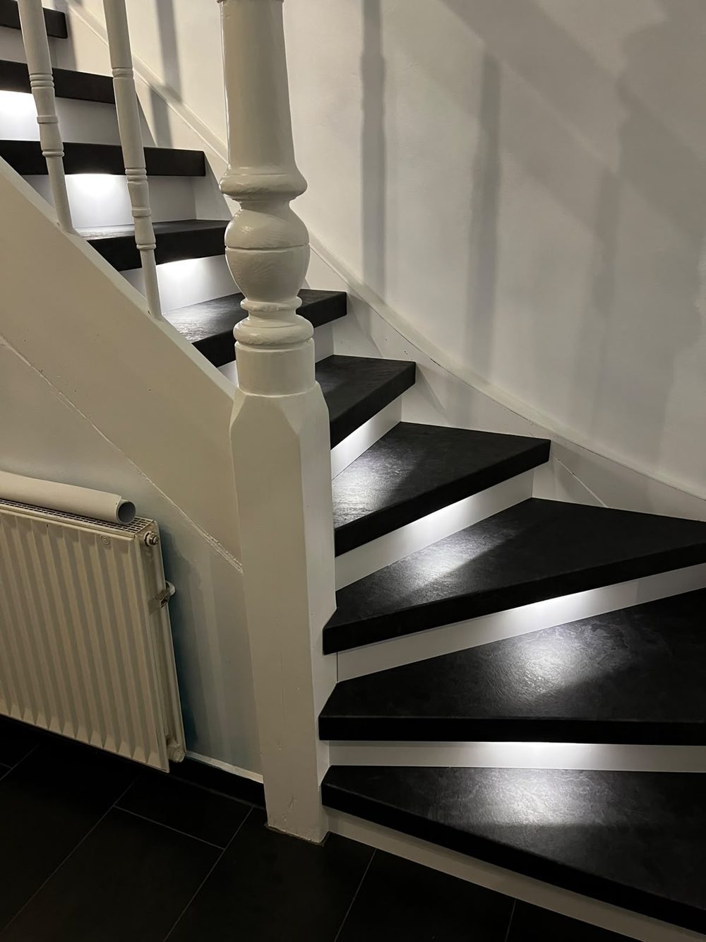 Die renovierte Treppe mit dunklen Stufen, weißen Stellstufen und weiß lackiertem Geländer